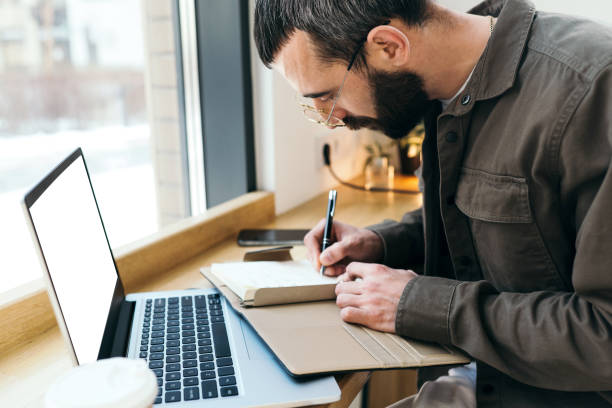 istock A caucasian man write in notepad on a cafe. work process. A man with a beard in a shirt is sitting in a cafe with a laptop, remote work, freelance 1475067729