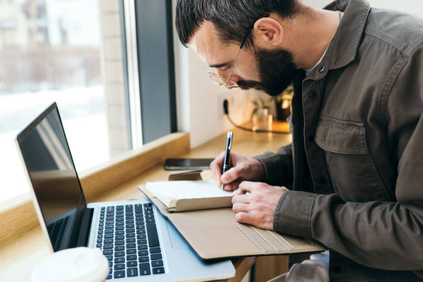 istock A caucasian man write in notepad on a cafe. work process. A man with a beard in a shirt is sitting in a cafe with a laptop, remote work, freelance 1475067730