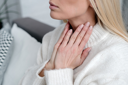 cropped shot of female feeling discomfort and touching inflamed throat with hands, girl in sweater checking thyroid gland, tonsillitis or thyroiditis concept