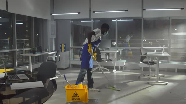 African-American janitor in facemask mop floor in empty office