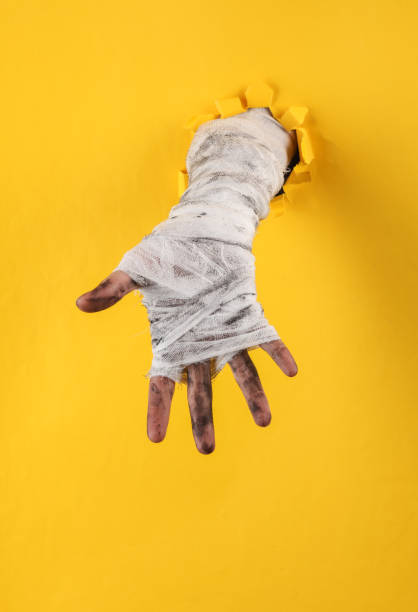 istock Mummy's hand in bandages through a torn hole in yellow paper 1475075231