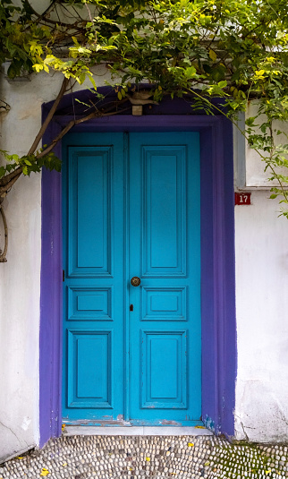 Old blue wooden door with violet frame in white wall. European architectural exterior poster.