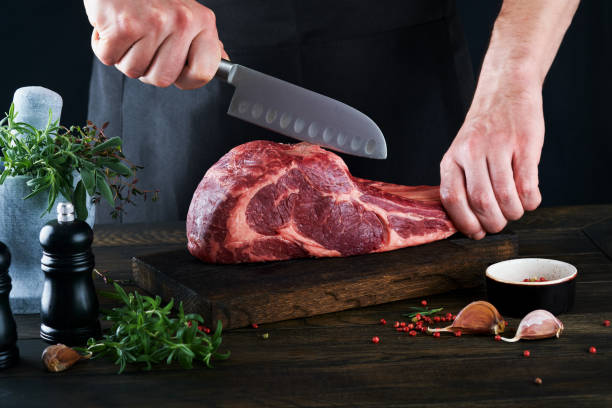 istock Chef cutting steak beef. Mans hands hold raw steak Tomahawk on rustic wooden cutting board on black background. Cooking, recipes and eating concept. Selective focus. 1475081135