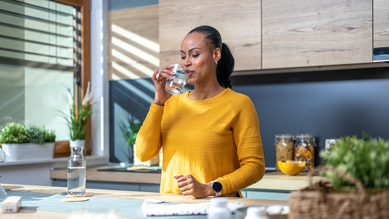 Mature woman taking medicine while standing in domestic kitchen.