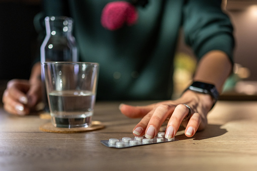 Woman's hands holding pills blister pack on table.