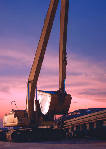 bagger und lastkahn warten auf die entladung im hafen gegen den dämmerungshimmel nach sonnenuntergang in vertikalem rahmen - industrial ship earth mover barge yellow stock-fotos und bilder