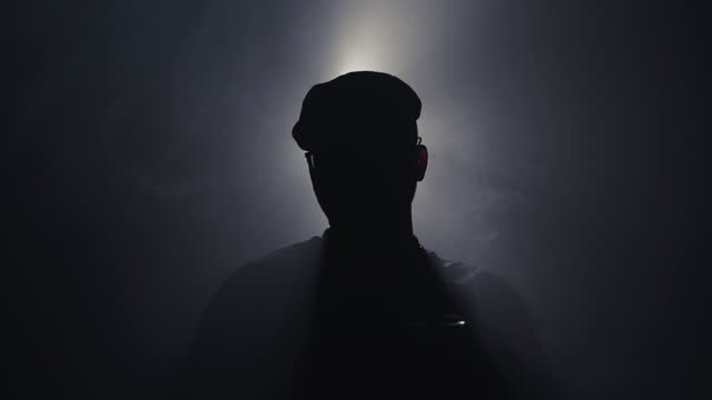 Mysterious businessman with hat holding a glass of drink backlit by cine background light and scene with smoke moving in slow motion