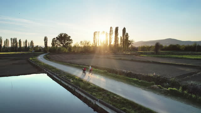 Family cycling together on rural road at sunrise, sunset, aerial drone shot