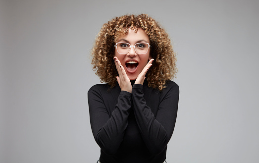 Young woman with curly hair and glasses in shock with happiness.
