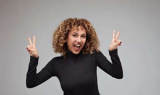 Young woman with curly hair smiling while making peace sign.