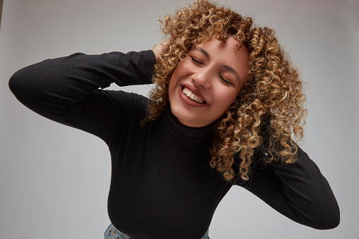 Portrait of happy woman with curly hair laughing leaning towards camera with hands in hair.