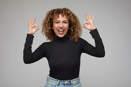 Cute young woman with curly hair making a hand gesture saying everything is fine.