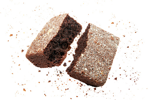A piece of a chocolate brownie glazed with white coconut frosting snapped in half floating in mid air with crumbs around, studio shot isolated on white background