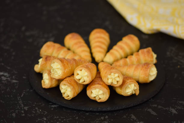 involtini ripieni di crema alla vaniglia sul piatto nero. - cream horn foto e immagini stock