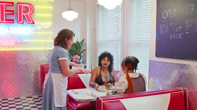 Waitress Serving An Order To Two Non-Binary People In 1950s Styled Diner