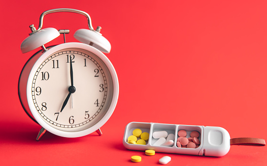 Time for health check concept. White alarm clock with pills, against the backdrop of Viva Magenta, copy space.