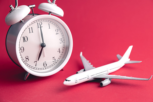 White alarm clock and airplane on the background of Viva Magenta, travel concept, copy space.