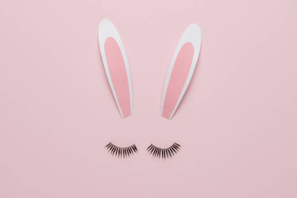 istock Minimal Easter concept. Bunny rabbit face made of paper bunny ears with eyelashes on pastel pink background. Flat lay. 1475102818