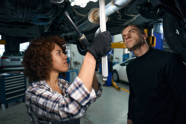 istock Young woman auto mechanic and client inspect car from below 1475104281