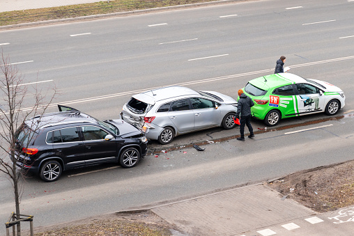 Riga, Latvia - February 15, 2023: Car crash accident with three cars on a city street. A drivers stand near wrecked cars and fill out documents for insurance.