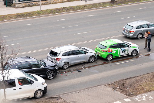 Riga, Latvia - February 15, 2023: Car crash accident with three cars on a city street. A drivers stand near wrecked cars and fill out documents for insurance.