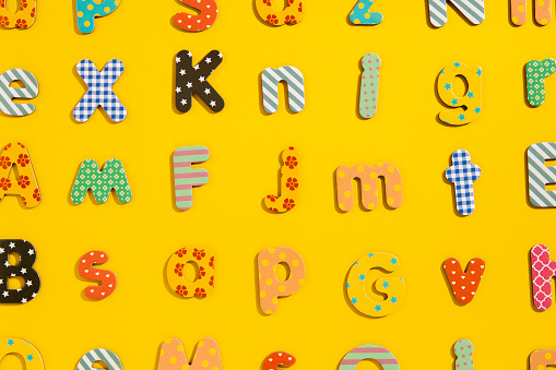Many multi-colored letters of the alphabet on a yellow background. Top view, flat lay.