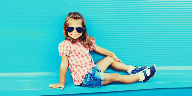 Summer portrait of little girl child wearing sunglasses, checkered shirt on blue background in the city stock photo