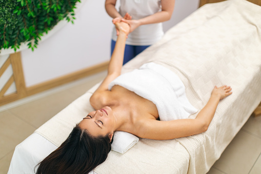 Happy woman receiving arm relaxational massage by professional therapist in beautiful spa center