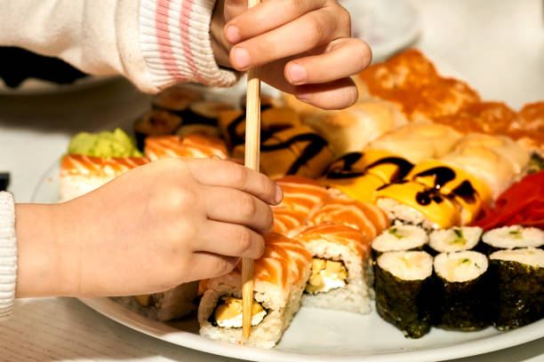 istock Children's hands taking delicious sushi with chopsticks. The child eats 1475112905