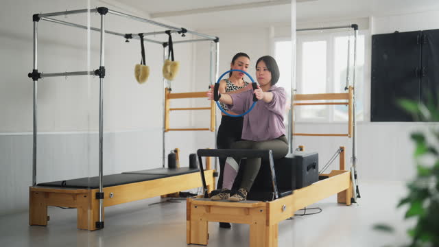Female pilates instructor demonstrating and showing how to train upper body to female student during pilates class