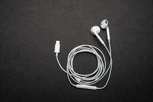 iPhone Apple Earpods, Airpods white earphones, headphones for listening to music and podcasts. Isolated black background. Budapest, Hungary - February 16, 2023