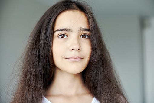 Serious beautiful preteen 12s girl pose indoors, having long brunette hair smile looking at camera. Generation Z or Alpha person portrait