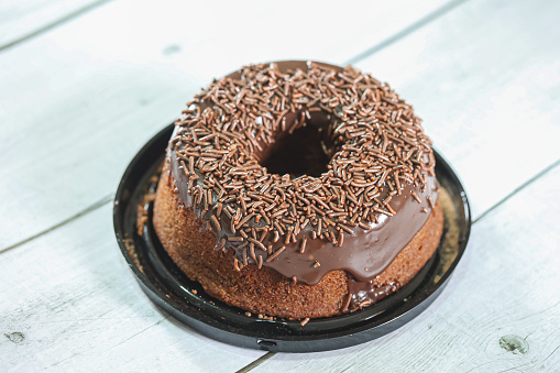 A chocolate cake with chocolate frosting and decorated with chocolate sprinkles. In Brazil it is known as bolo de brigadeiro. Wooden table.