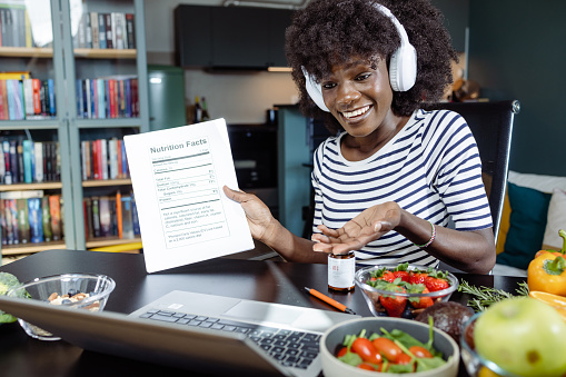 Portrait of a young African American nutritionist with wireless headphones talking online with a client.  She is explaining nutrition basics while holding a plan.
