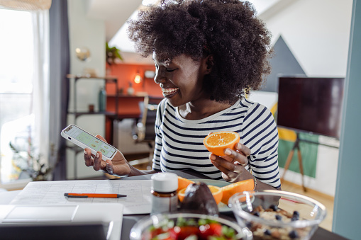 A young African American woman is checking nutrition value and calories intake via a diet tracker app on smart phone