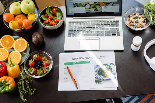 High-angle view of nutritionist doctor's desk. A laptop, a nutrition plan and a variety of fruits and vegetables are on the desk