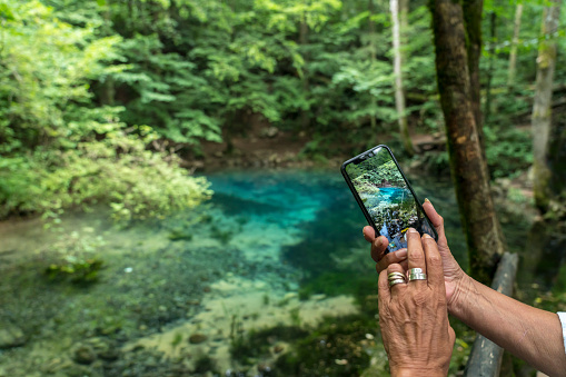 The blue waters of Stifone on the Nera River in National park Nera-Beusnica. Visible hands holding mobile phone taking photo of the river.