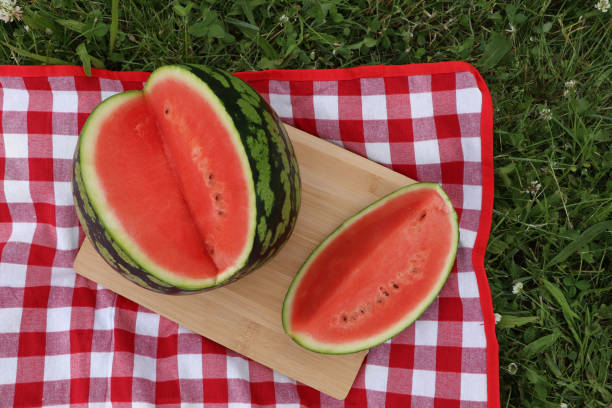 istock Delicious cut watermelon on red checkered blanket outdoors, top view 1475124408