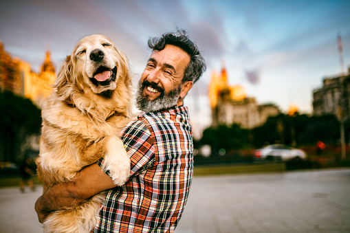 Mature man hugs golden retriever in city park