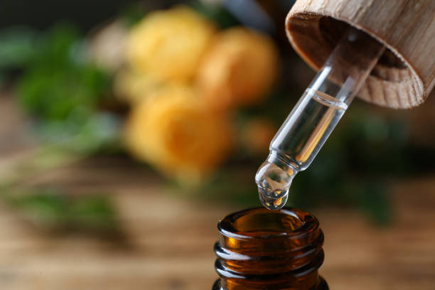 istock Dripping rose essential oil from pipette into bottle on blurred background, closeup. Space for text 1475126765