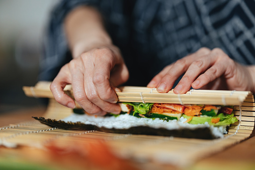 An anonymous Asian female chef preparing sushi on a bamboo mat at home.
