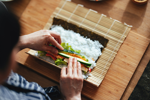 High angle view of an anonymous Asian female chef preparing sushi on a bamboo mat at home.