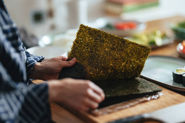 Close Up Photo Of Woman Hands Holding Nori Sheets High angle view of an anonymous Asian female chef holding nori seaweed sheets and preparing a healthy meal at home. nori stock pictures, royalty-free photos & images