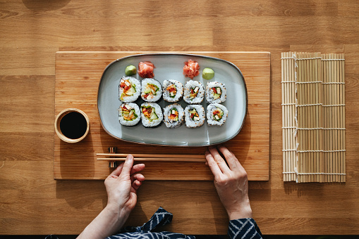 Directly above photo of an anonymous Asian female chef putting chopsticks on the table next to the plate with sushi and bowl with soy sauce.