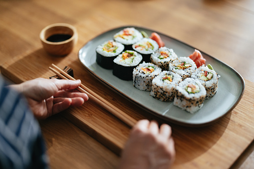 High angle view of an anonymous Asian female chef putting chopsticks on the table next to the plate with sushi and bowl with soy sauce.