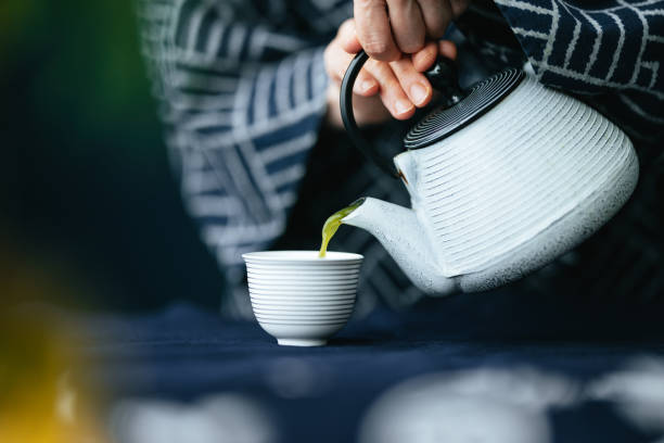 nahaufnahme von frauenhänden, die matcha-grüntee aus der teekanne in eine tasse gießen - matcha tee stock-fotos und bilder