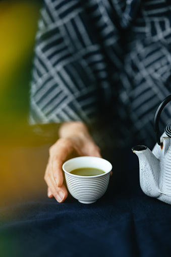 High angle view of an anonymous Asian woman in kimono preparing cup of hot tea at kitchen desk.