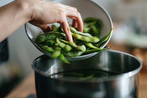 Close Up Photo Of Woman Hands Adding Edamame To The Pot In The Kitchen