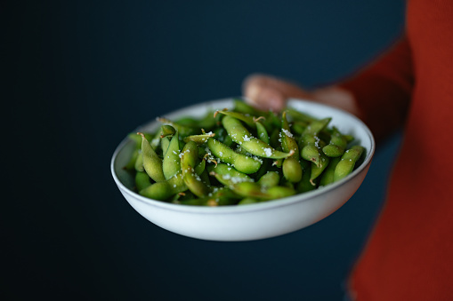 An anonymous Asian female chef serving edamame beans snack at home.