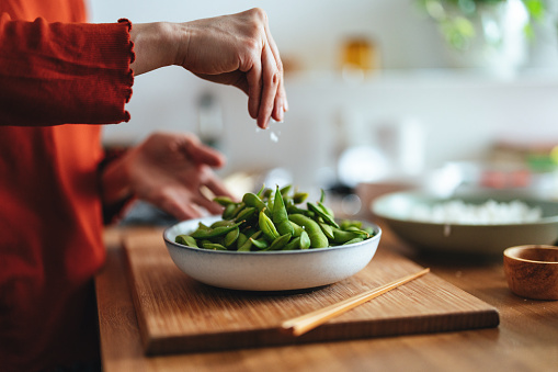An anonymous Asian female chef preparing edamame beans snack in the kitchen.